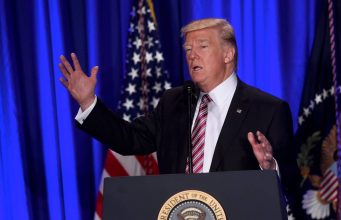 Donald J. Trump’s First 100 Days Donald Trump standing on a stage in front of a curtain